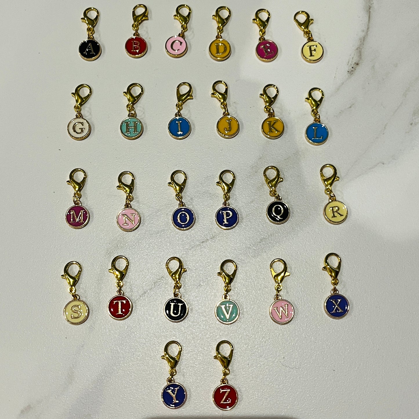 petites breloques en email de couleurs différentes avec l'initiale en doré avec un mousqueton doré