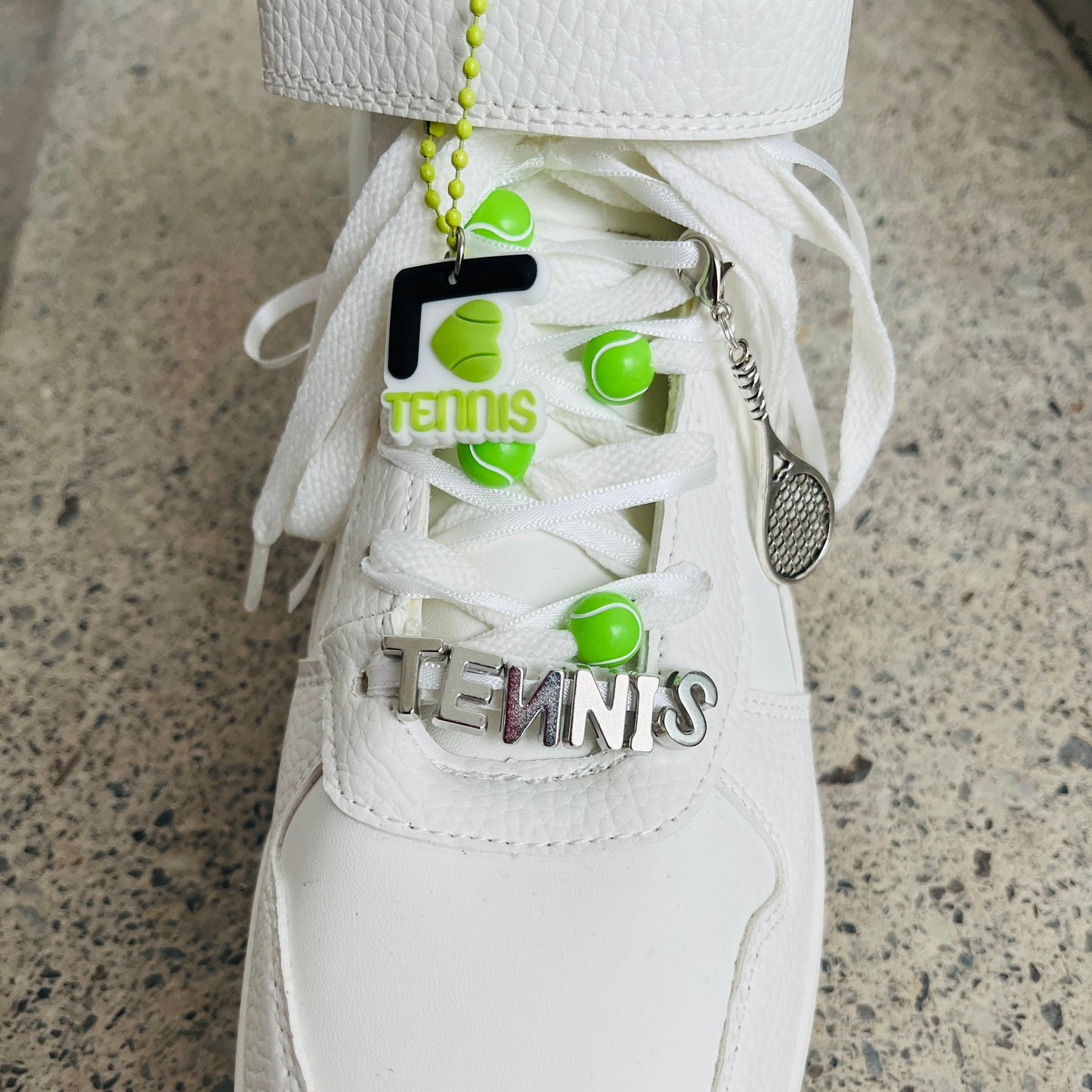 une basket avec un Pack BIJOUX charms raquettes de Tennis fixées sur les lacets blancs et rubans blancs avec balles de tennis et lettres tennis argentées