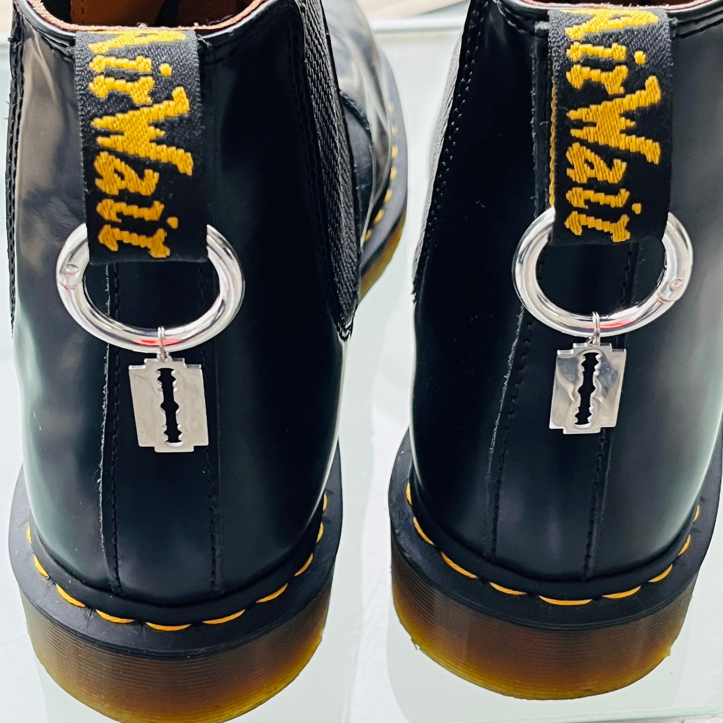 Une paire de Dr Martens avec des anneaux et une lame de rasoir accrochée à l'arrière de la chaussure