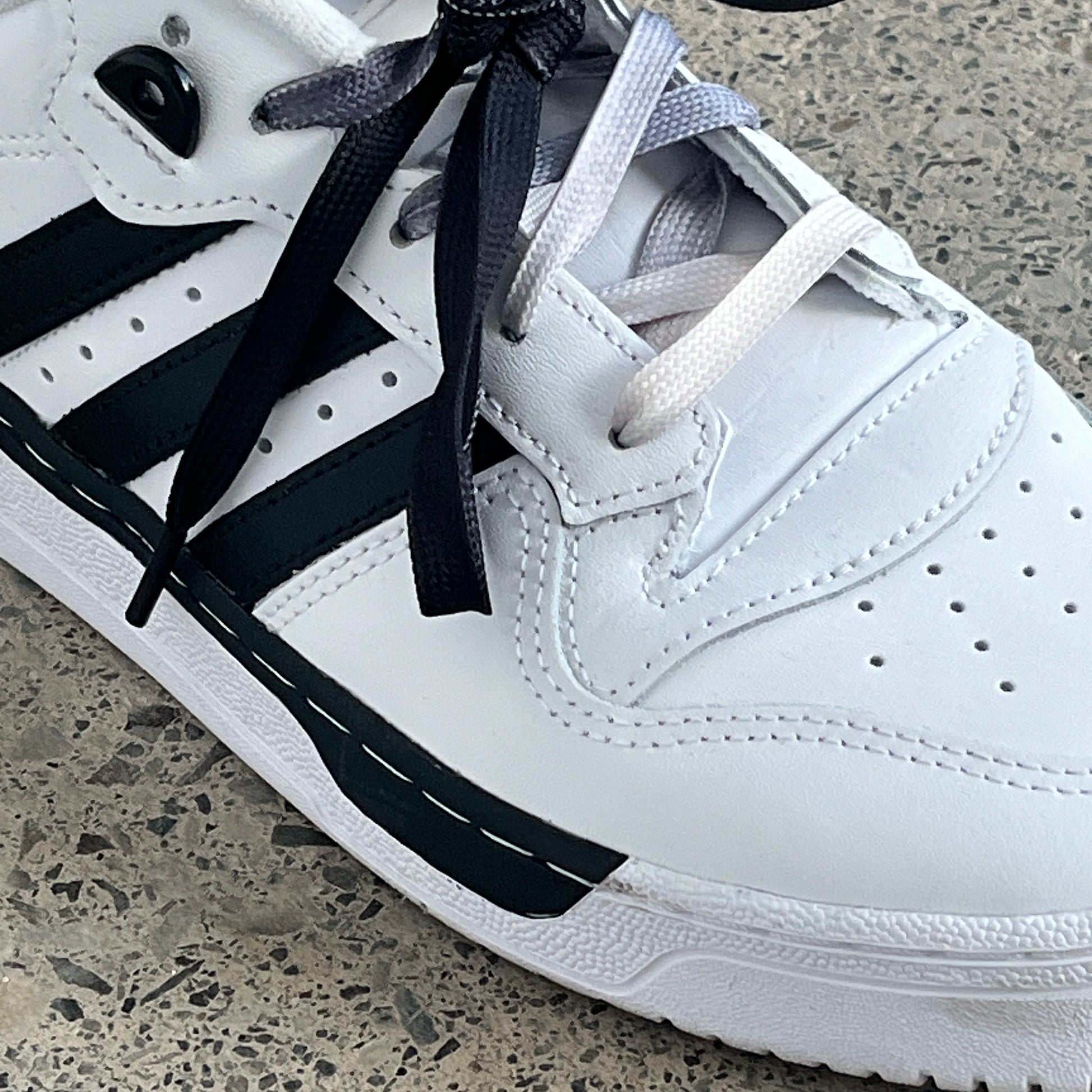 Une basket blanche et noir avec un lacet dégradé de noir
