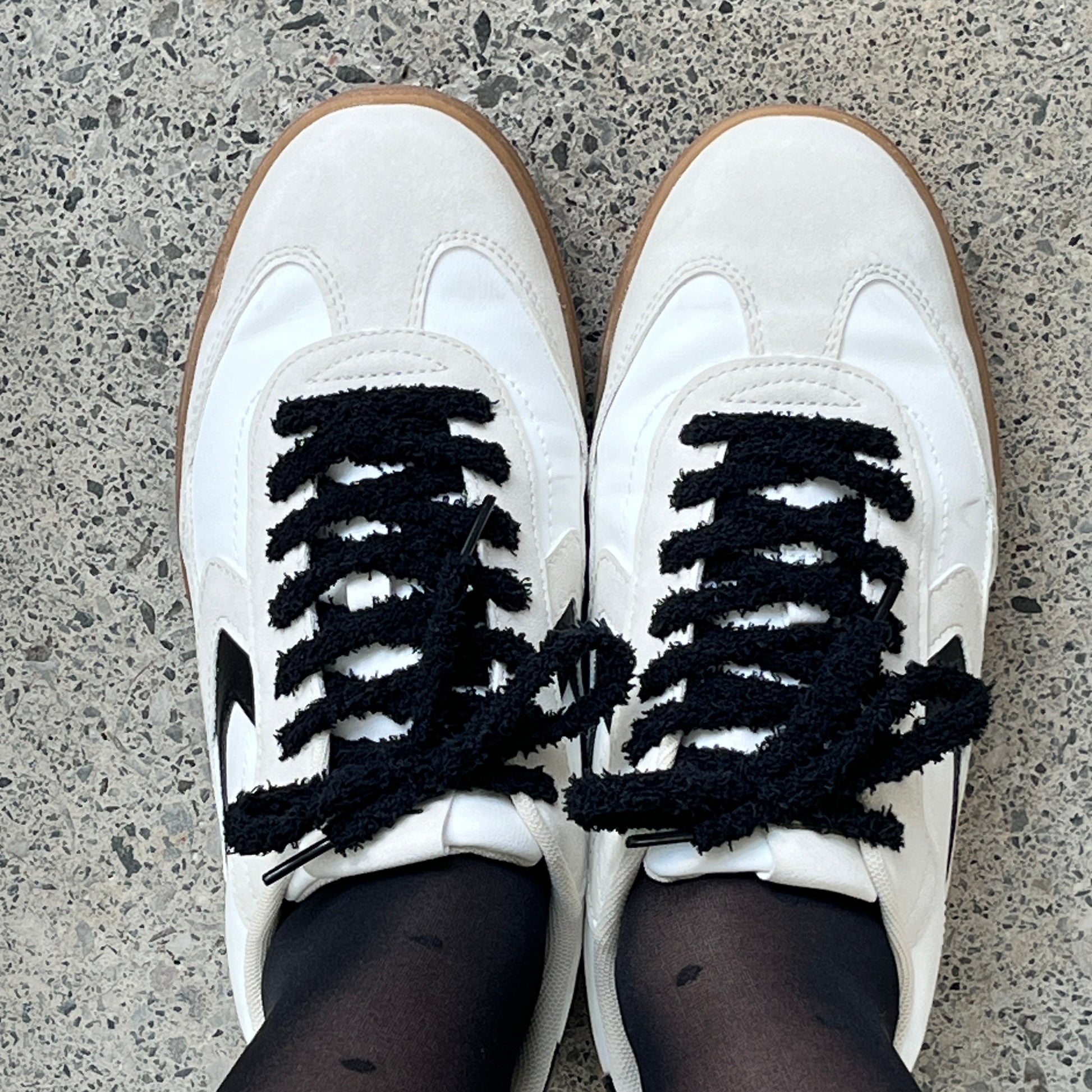 une paire de baskets blanches avec des lacets pilou pilou noirs