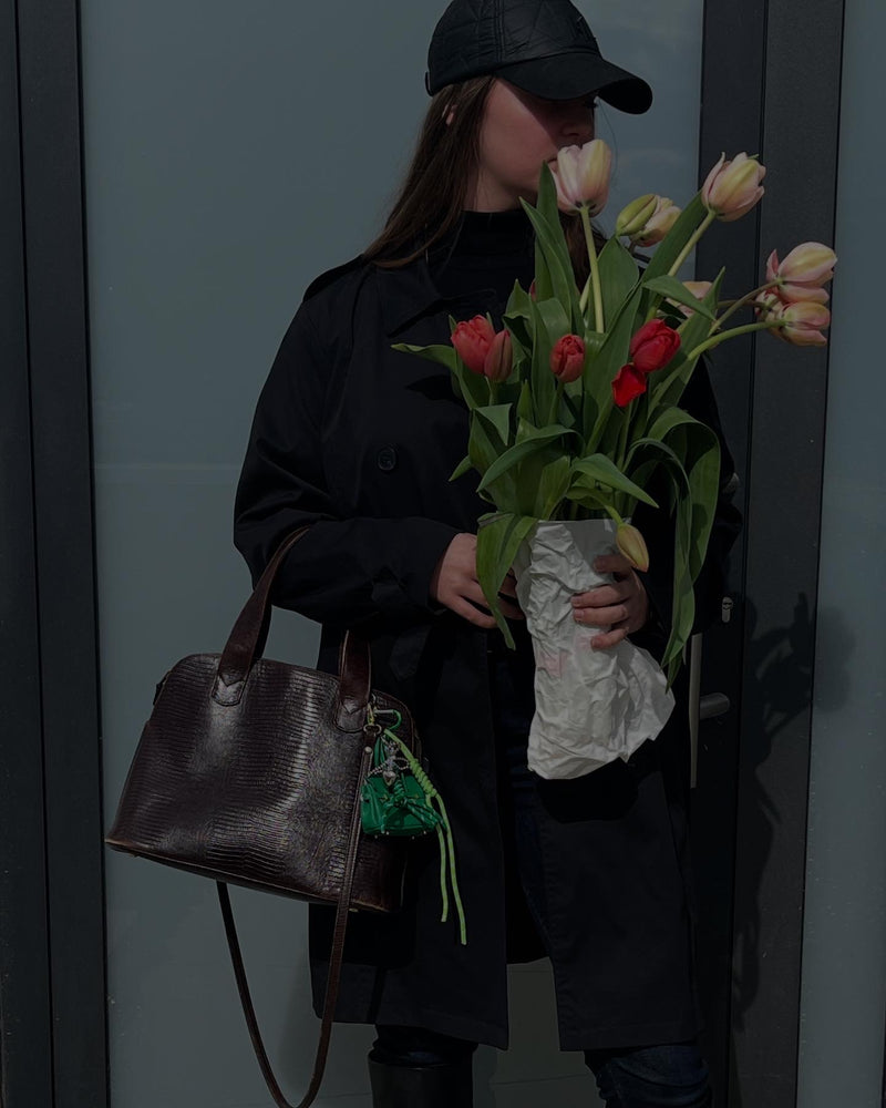 mini sac vert accroché à un sac marron en serpent au bras d'un mannequin portant un bouquet de tulipes
