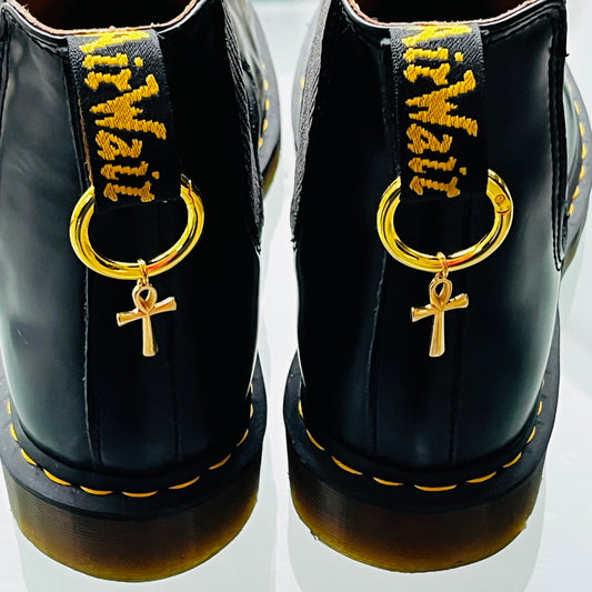 une paire de Dr Martens noires avec des anneaux et une croix égyptienne