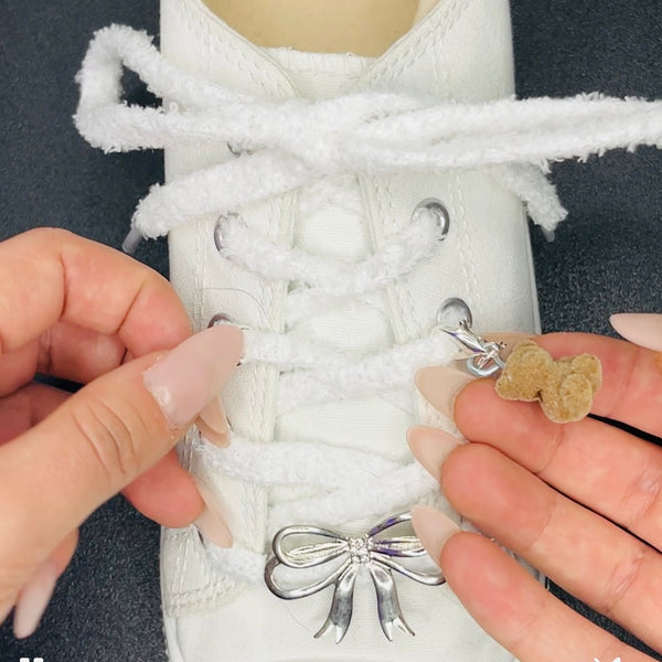 une converse avec des lacets flufy blancs et une breloque ours accroché au lacet et une barrette de chaussure en noeud