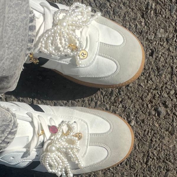 une paire de baskets avec des noeuds en perles et des breloques avec initiales