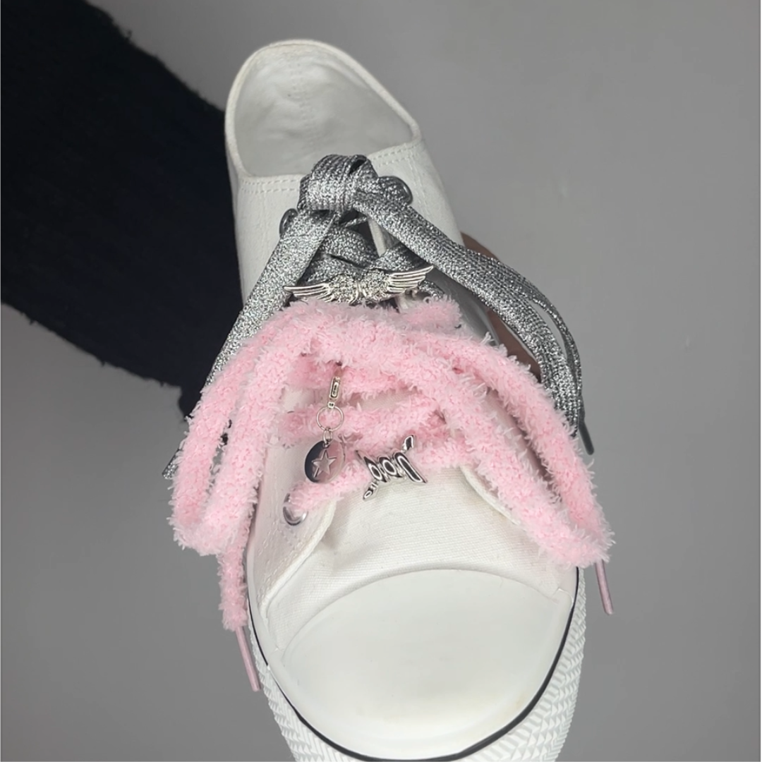 une converse avec un lacet rose et un lacet argenté une barrette aile d'ange et un barbelé