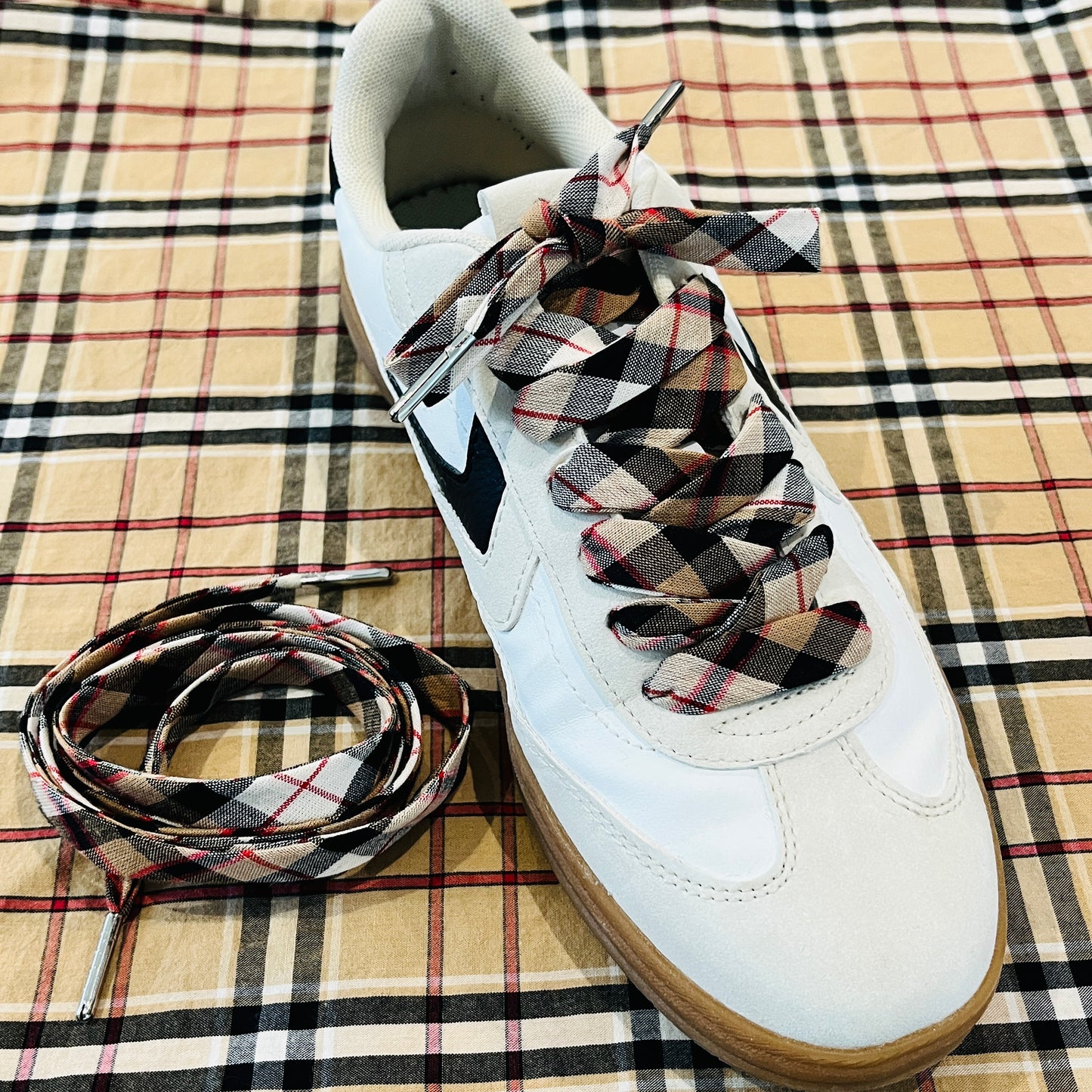 lacets tartan écossais mis sur des baskets posés sur un tissu à carreaux beige noir et rouge