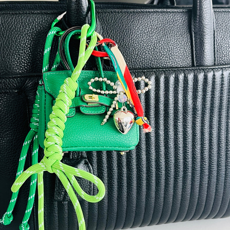 mini sac vert accroché à l'anse d'un sac noir avec un mousqueton vert et boots verts et couer argenté