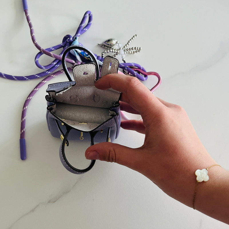 mini sac pour accrocher sur son sac à main de couleur parme qui s'ouvre et dans lequel on peut mettre des écouteurs un rouge à lèvre avec boots violets et coeurs argentés